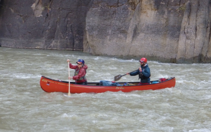 two people paddle a canoe through whitewater